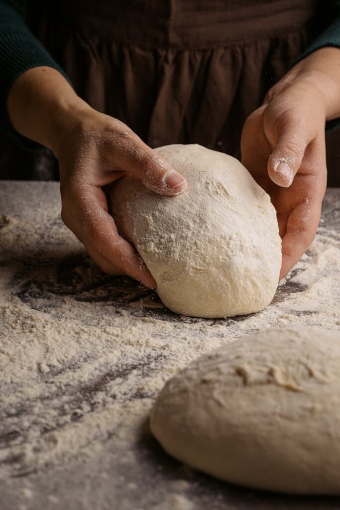 pexels-photo-10009354 A baker's hands kneading fresh dough on a floured surface for bread making.