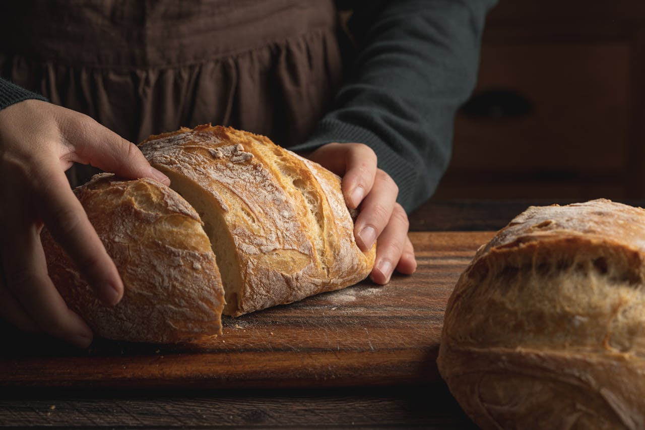 Close-up of hands holding a freshly baked crusty bread loaf on a wooden board.