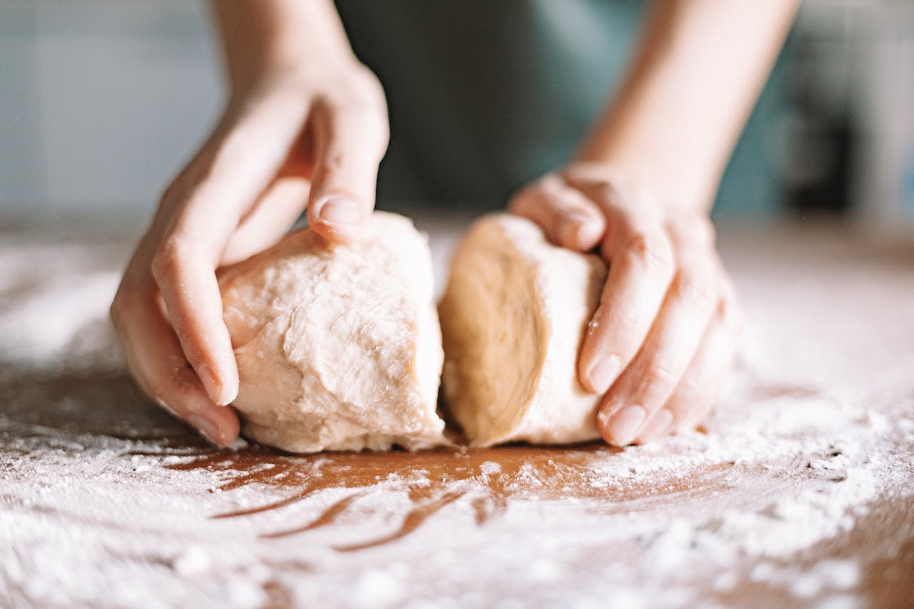 Close-up of hands kneading dough on a floured surface, showcasing food preparation indoors.